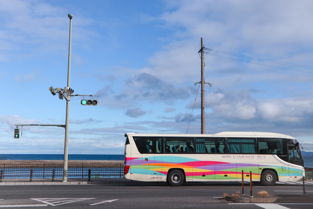 a multicolored bus driving down a street next to the ocean
