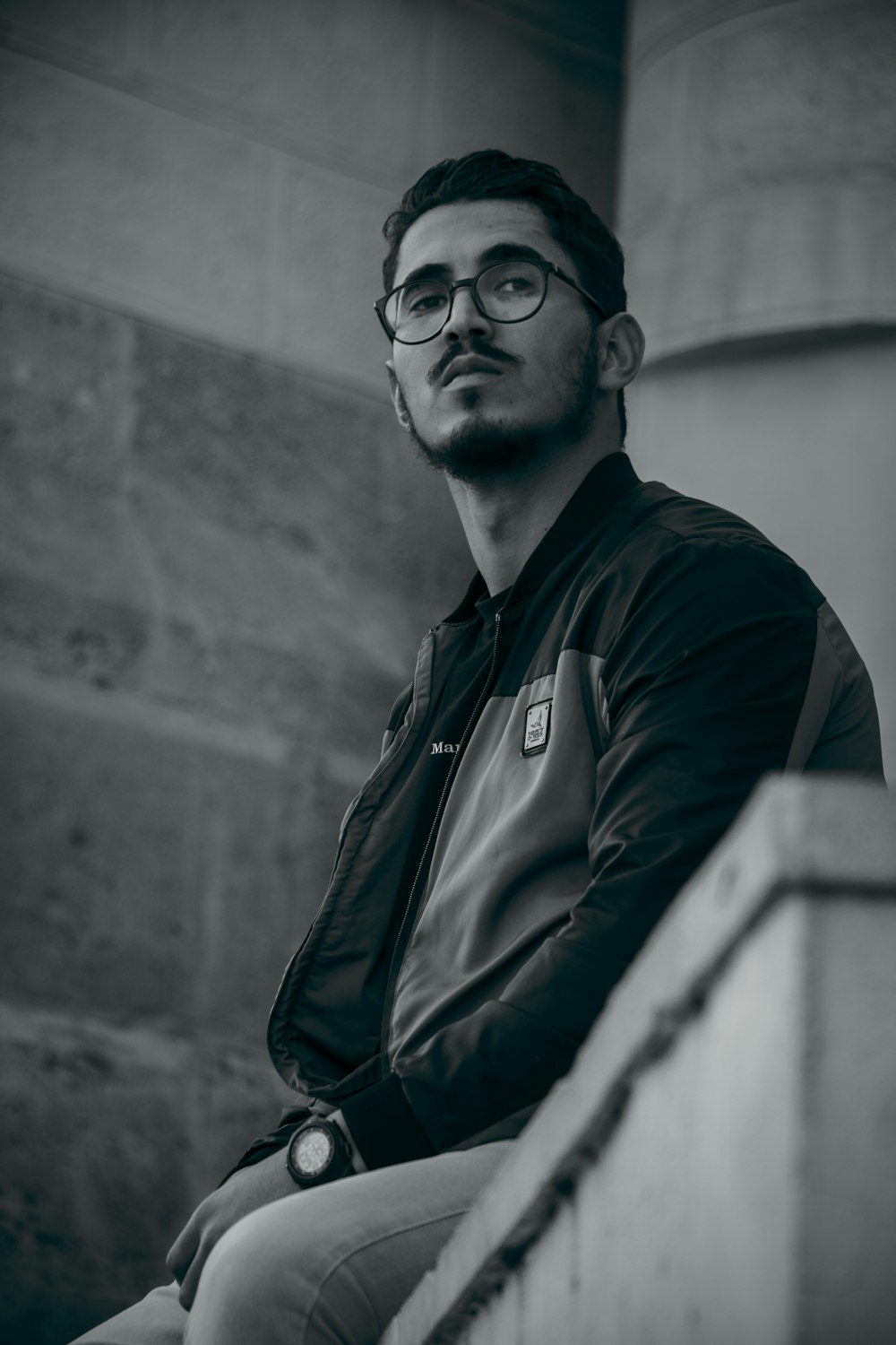 a man with glasses sitting on a ledge