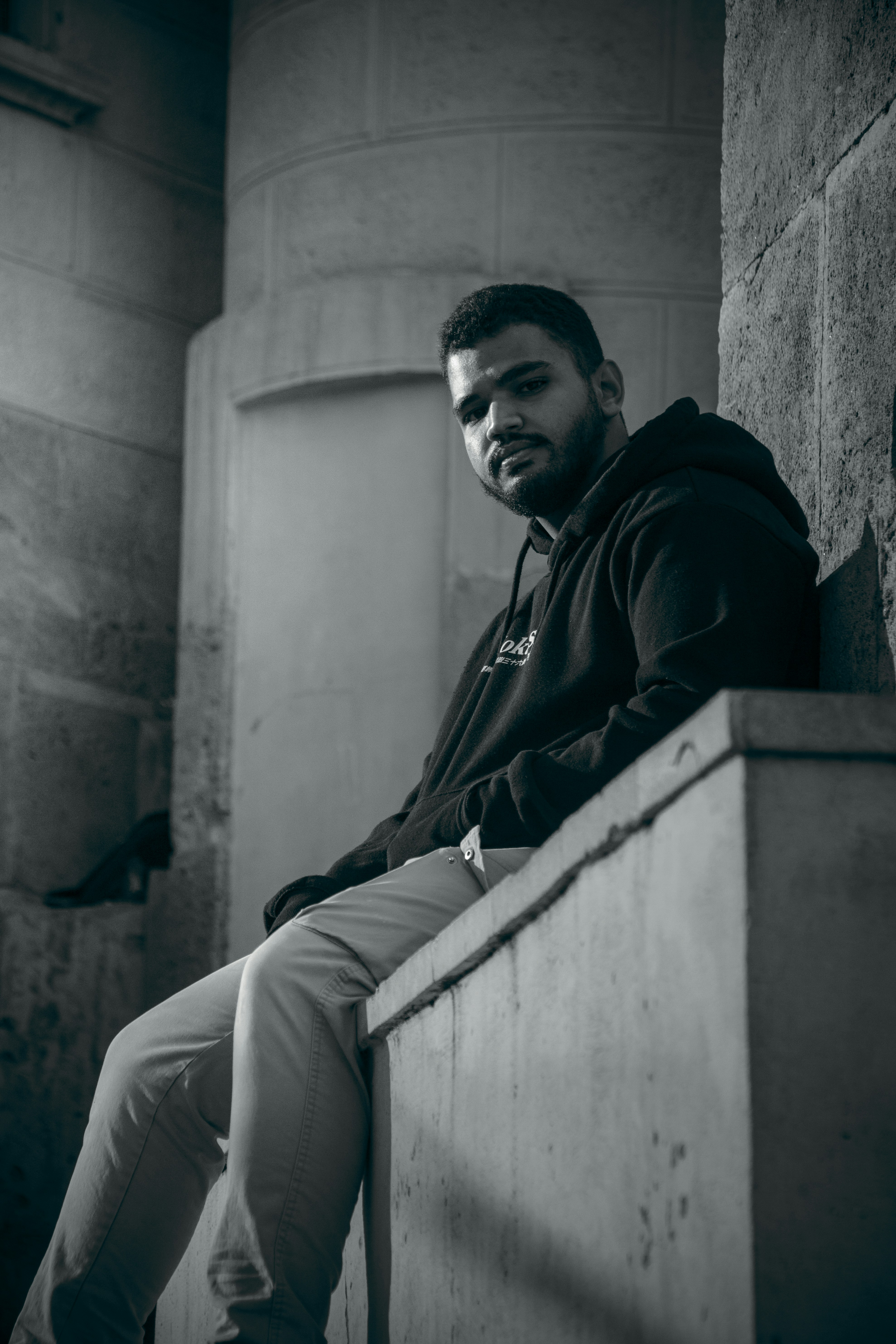 a black and white photo of a man sitting on a ledge