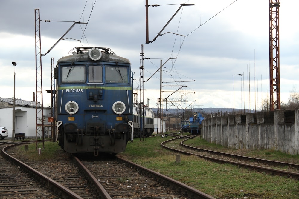 a blue train traveling down train tracks next to a building