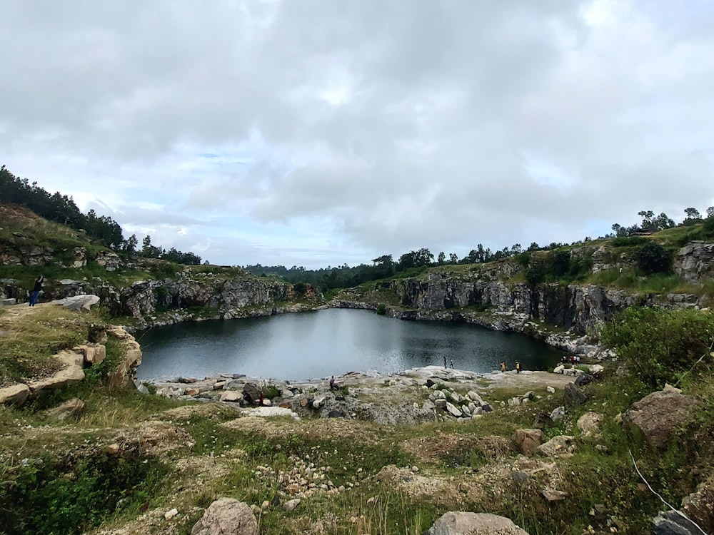 a lake surrounded by rocks and grass on a cloudy day
