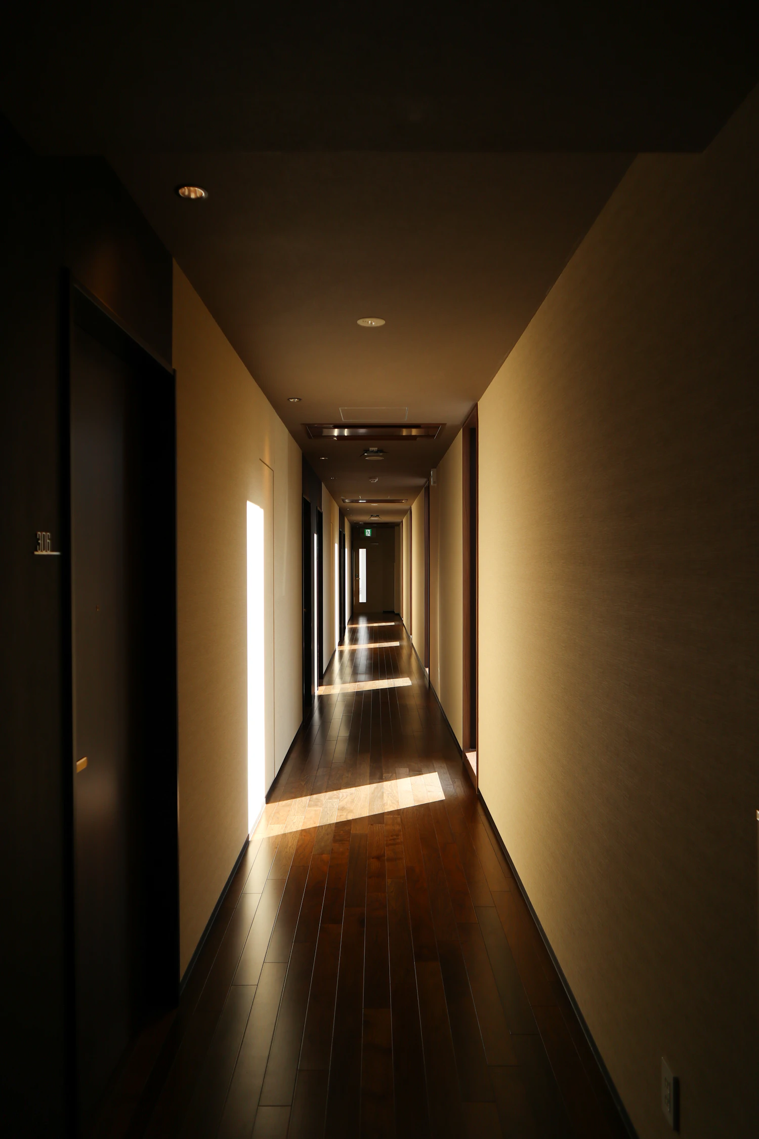 A corridor with a wooden floor cut into stripes by light from side windows