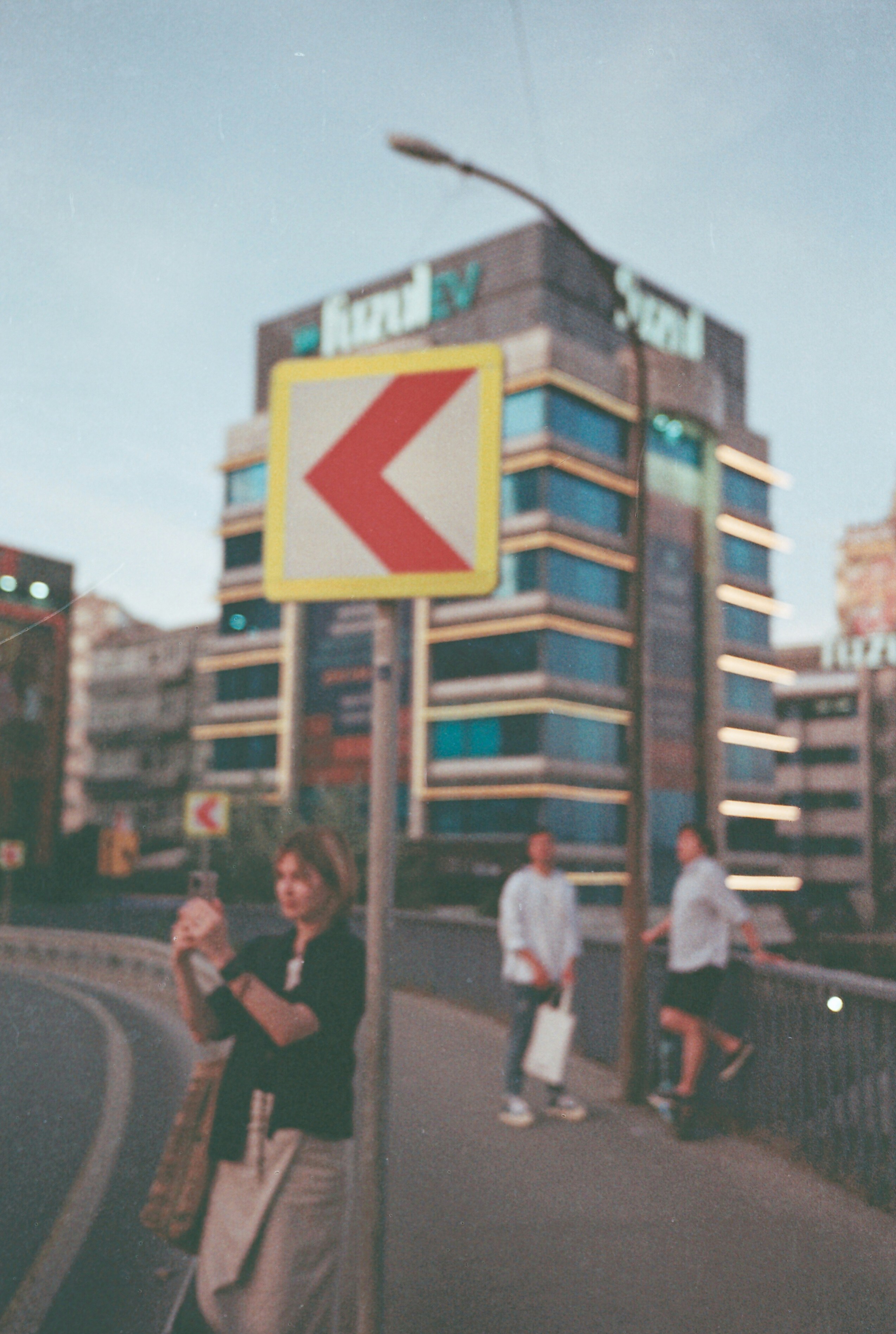 a woman standing on the side of a road next to a street sign