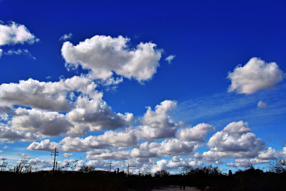 a blue sky with white clouds and a person walking down the road