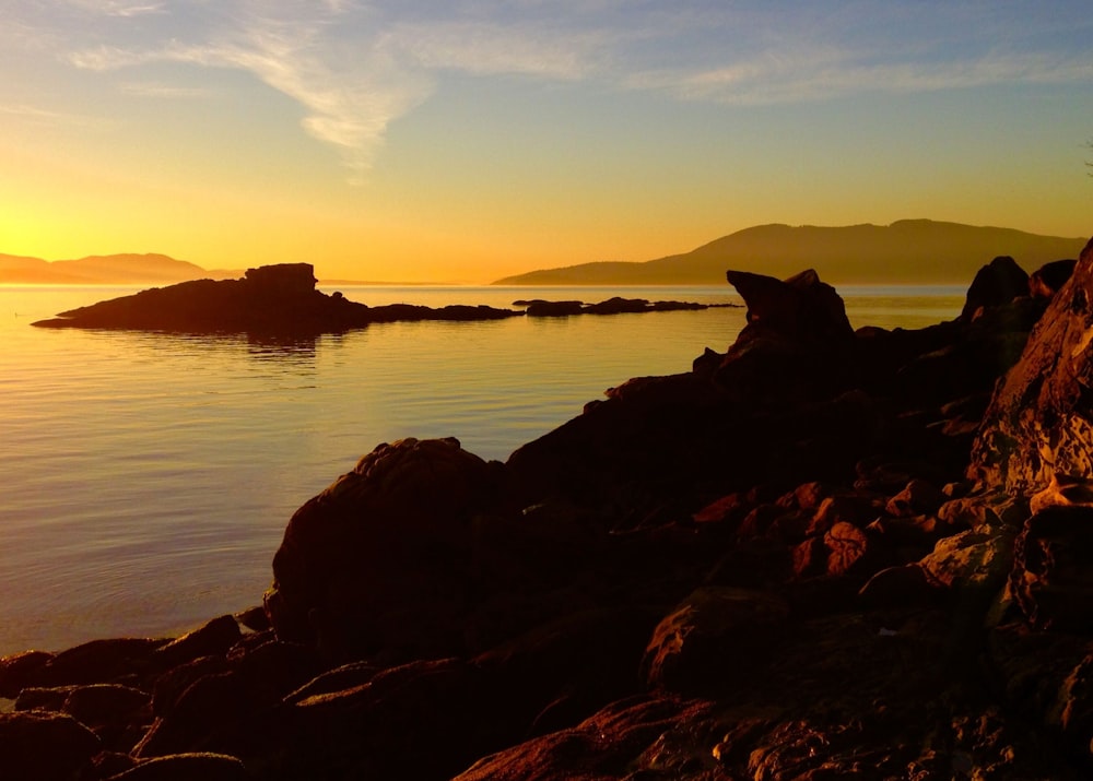 the sun is setting over the water and rocks