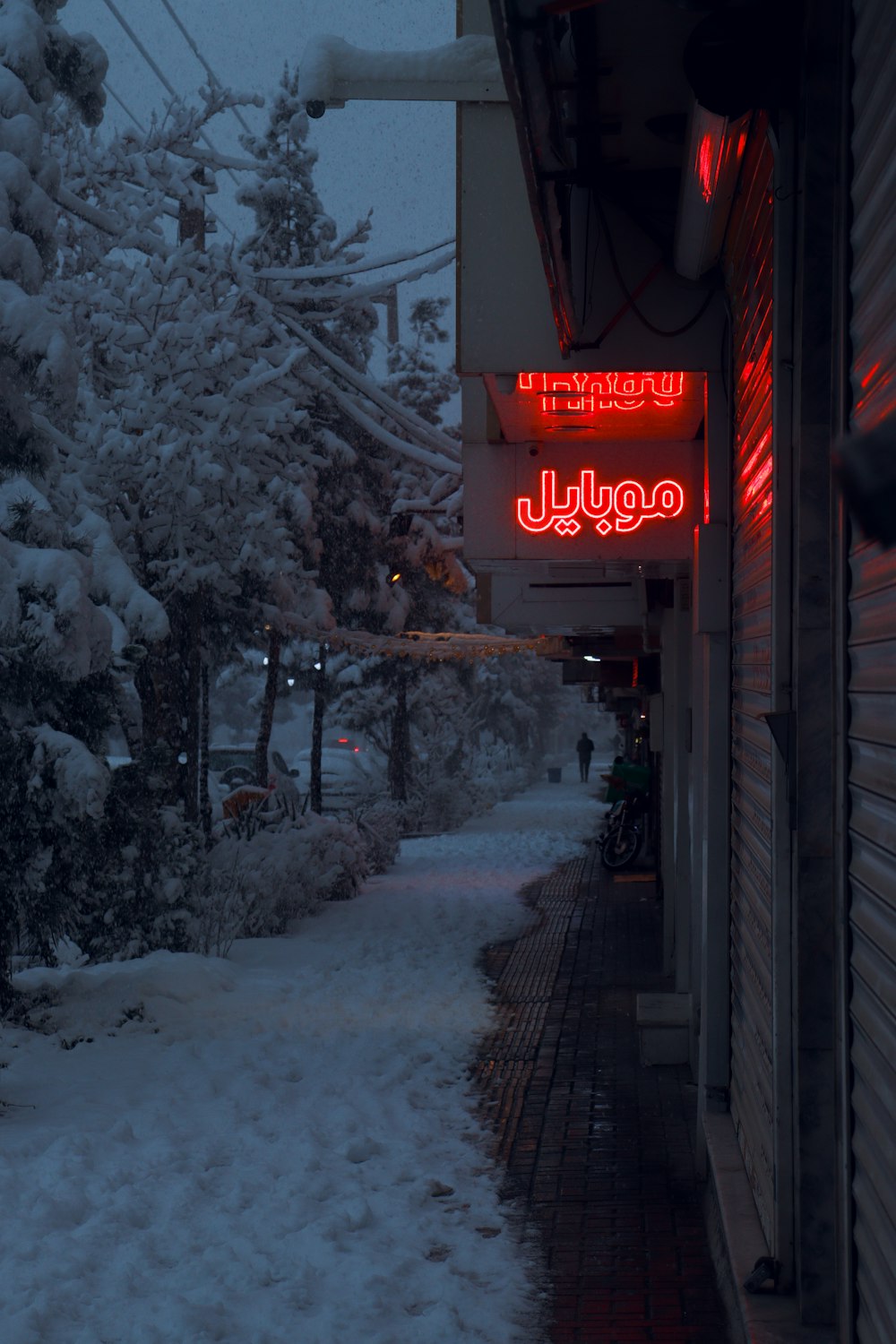 a snowy sidewalk with a red neon sign on it