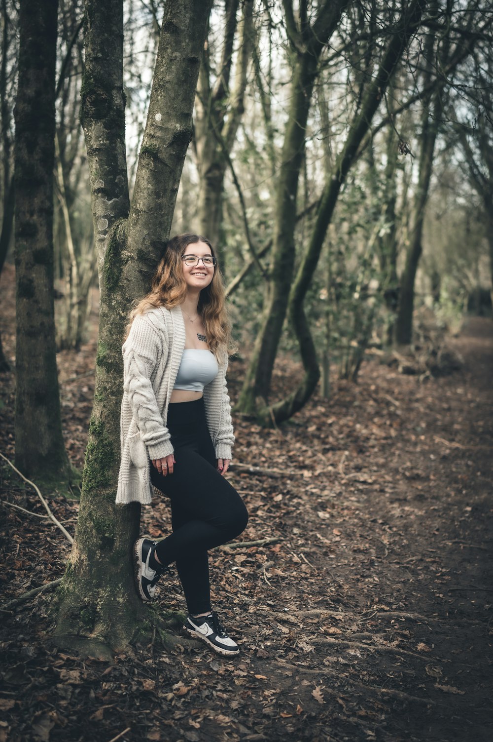 a woman standing next to a tree in a forest