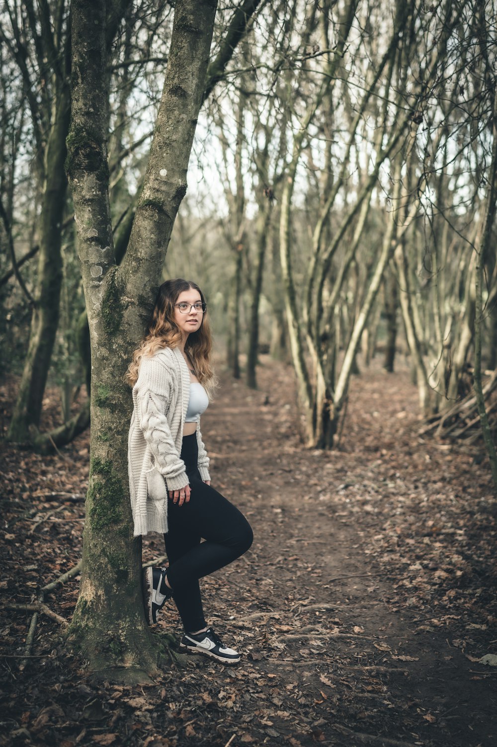 une femme appuyée contre un arbre dans une forêt