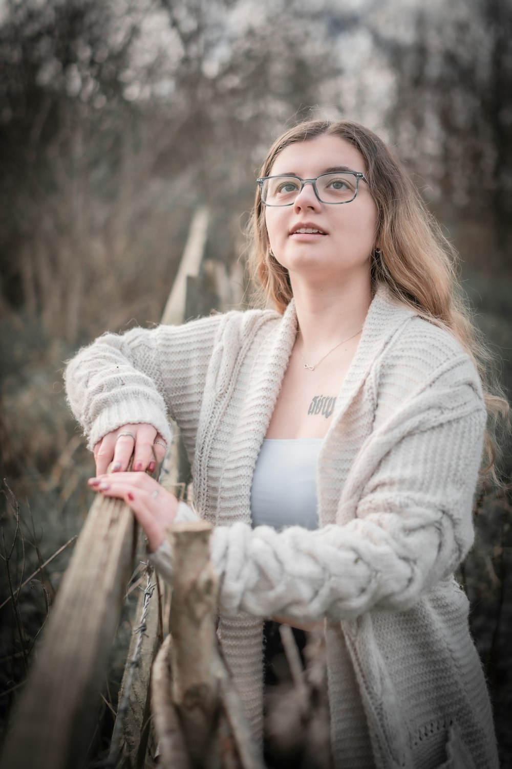 a woman wearing glasses leaning on a fence