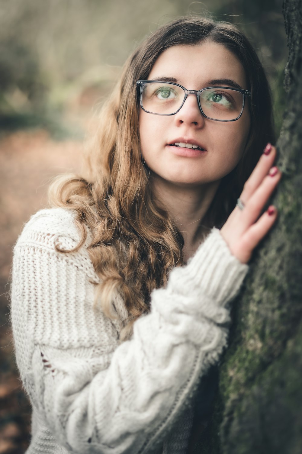 a woman wearing glasses leaning against a tree