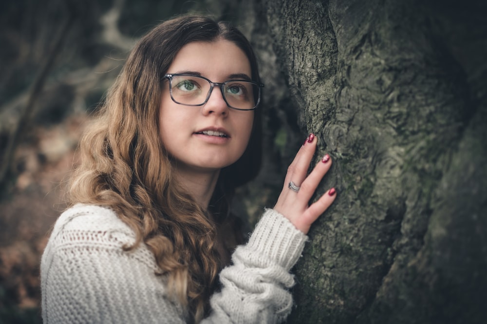 a woman wearing glasses leaning against a tree