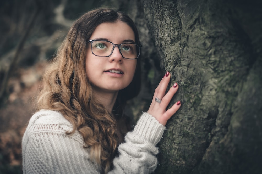 une femme portant des lunettes appuyée contre un arbre