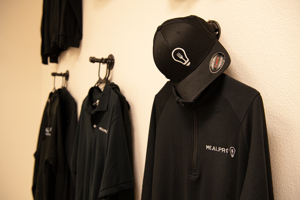 a black hoodie hanging on a wall next to a row of black shirts