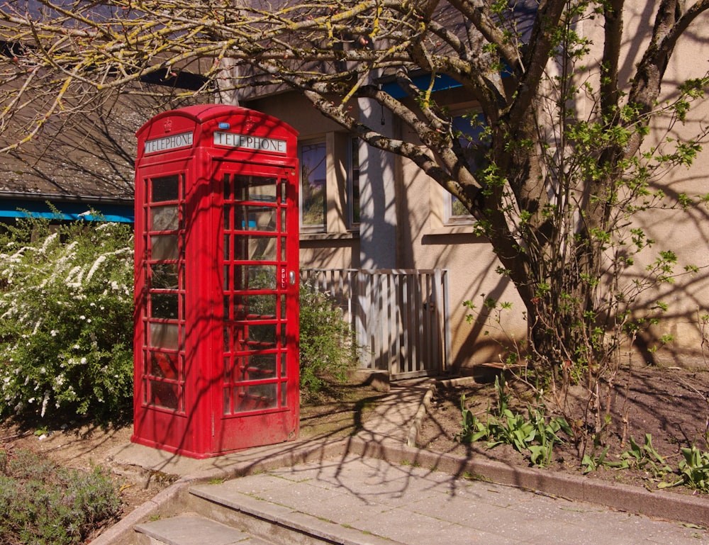 a red phone booth sitting next to a tree