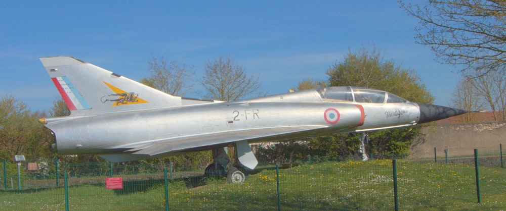 a silver fighter jet sitting on top of a lush green field