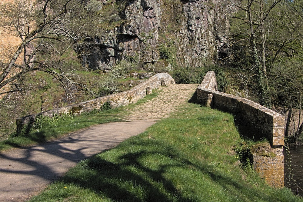 a stone bridge over a river next to a lush green hillside