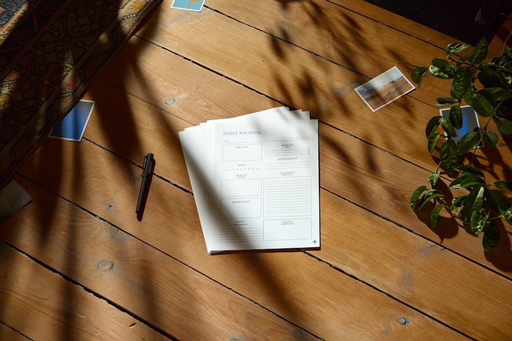 a wooden table topped with papers and a pen