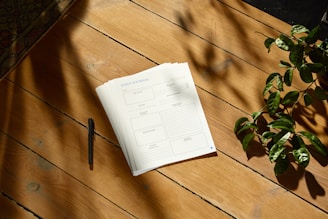 a notepad sitting on top of a wooden table next to a plant