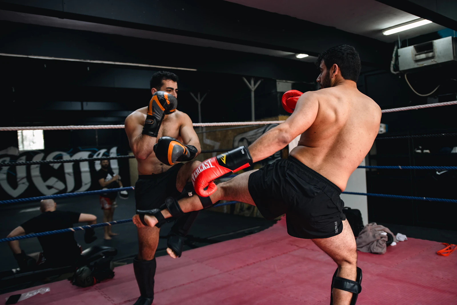 Two fighters sparring, one throwing a kick in a boxing ring