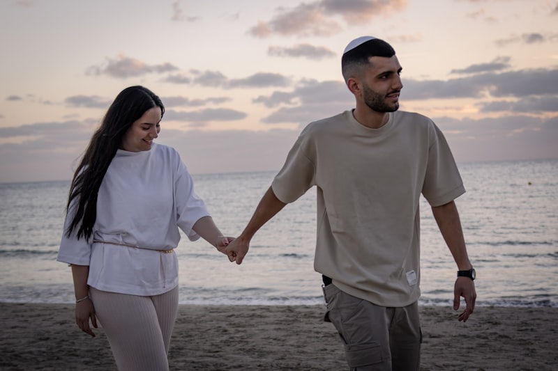 Couple in coordinated neutral outfits walking on beach at sunset