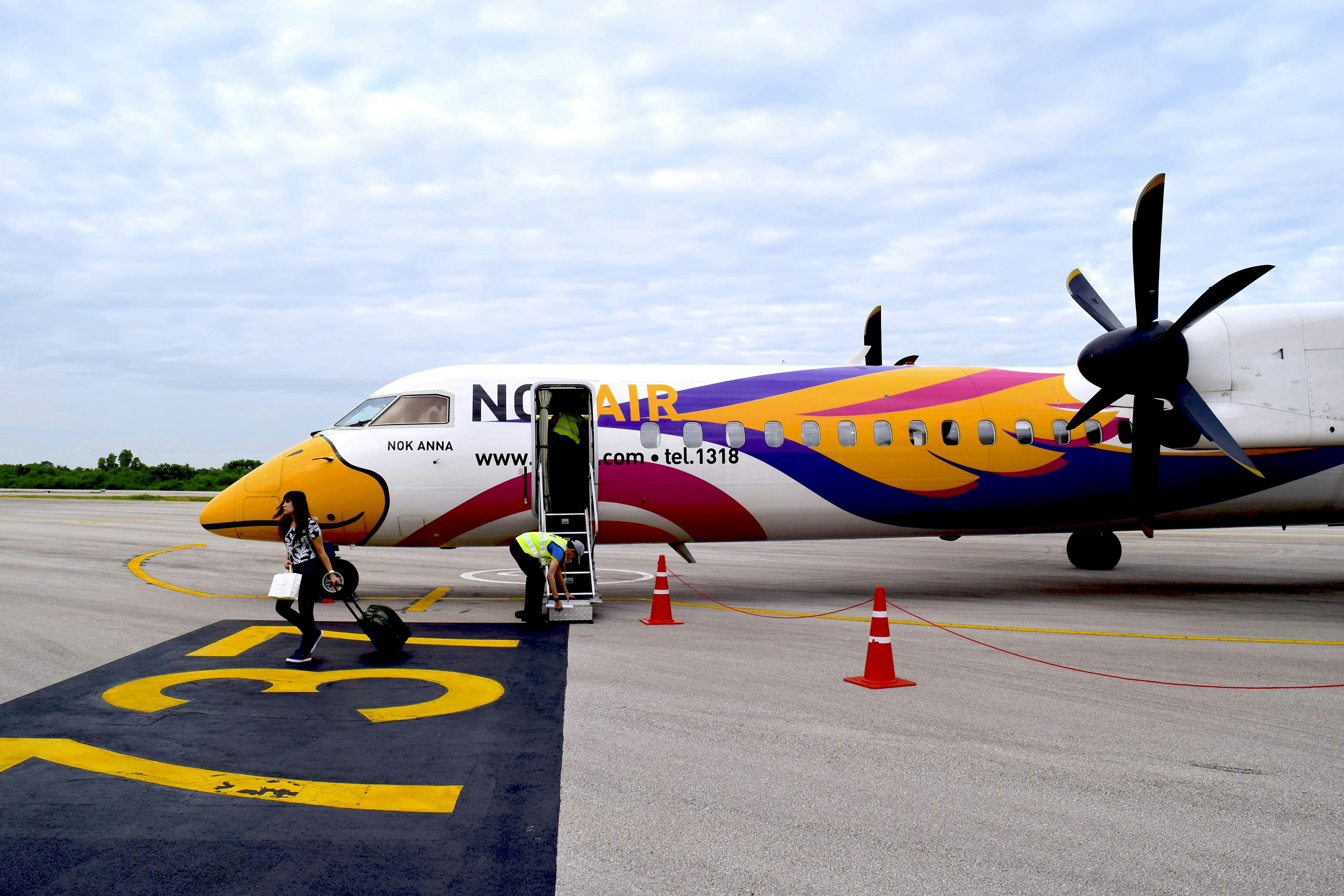 a man standing next to an airplane on a runway, The Q400 (HS-DQA) at Lampang Airport.