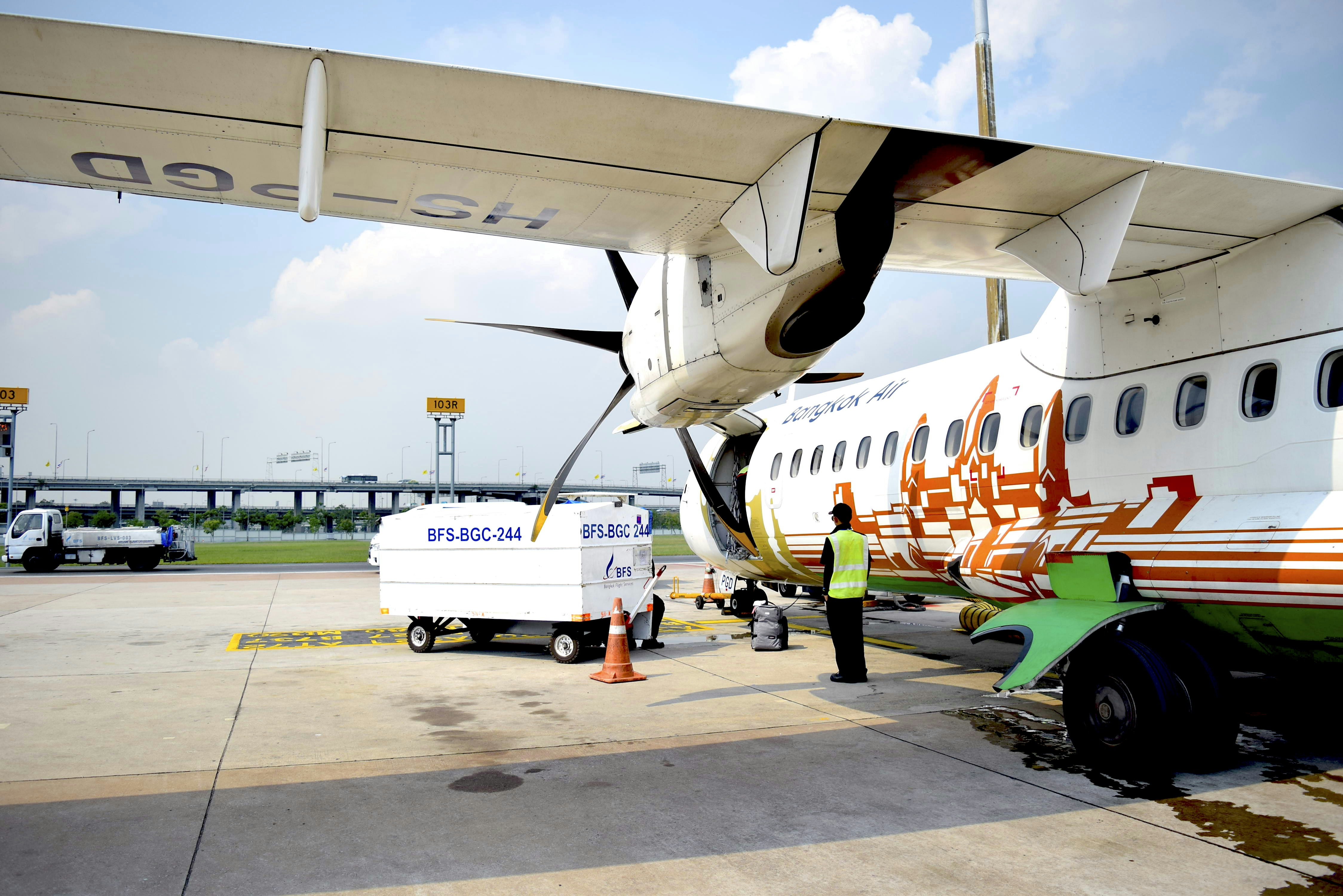 a man standing next to an airplane on a tarmac, BKP ATR72-500 (HS-PGD) on BKK ramp.