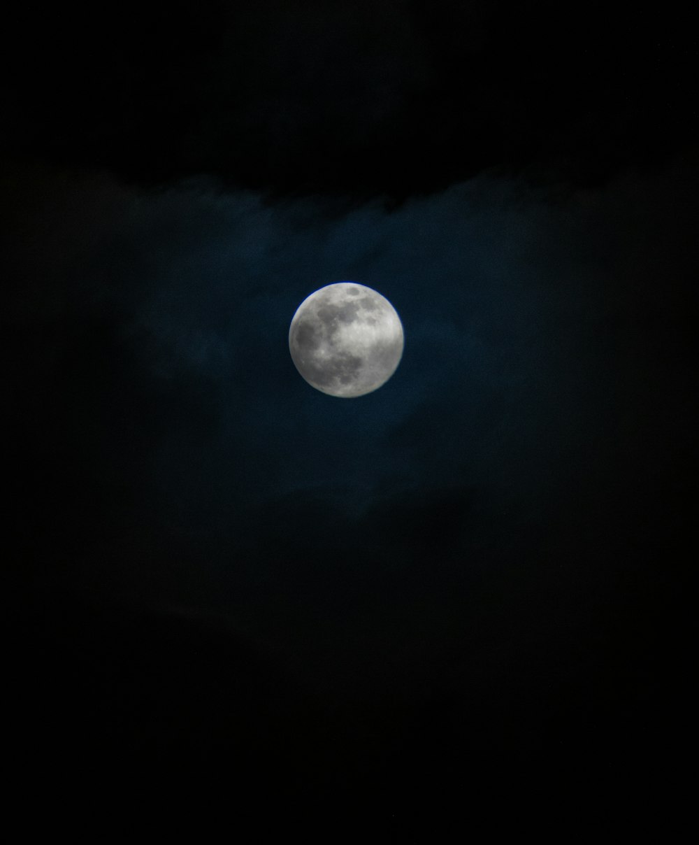 a full moon in the dark sky with clouds