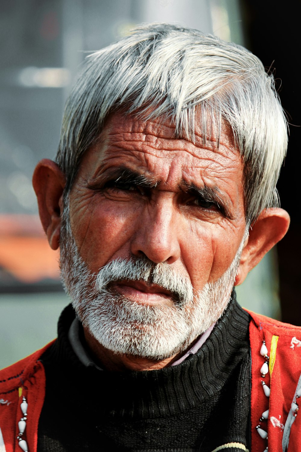 a man with white hair and a beard wearing a red vest