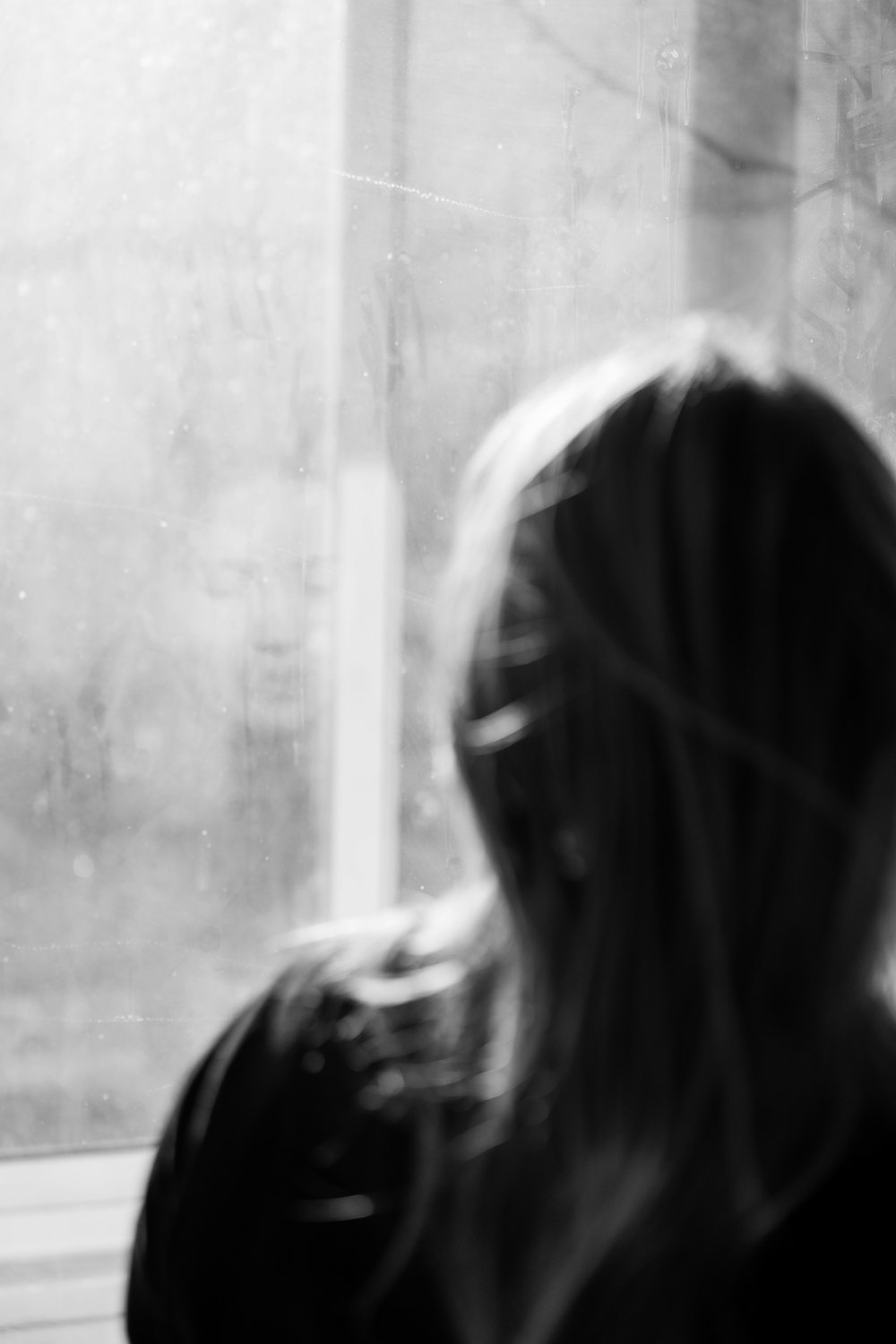 a black and white photo of a woman looking out a window