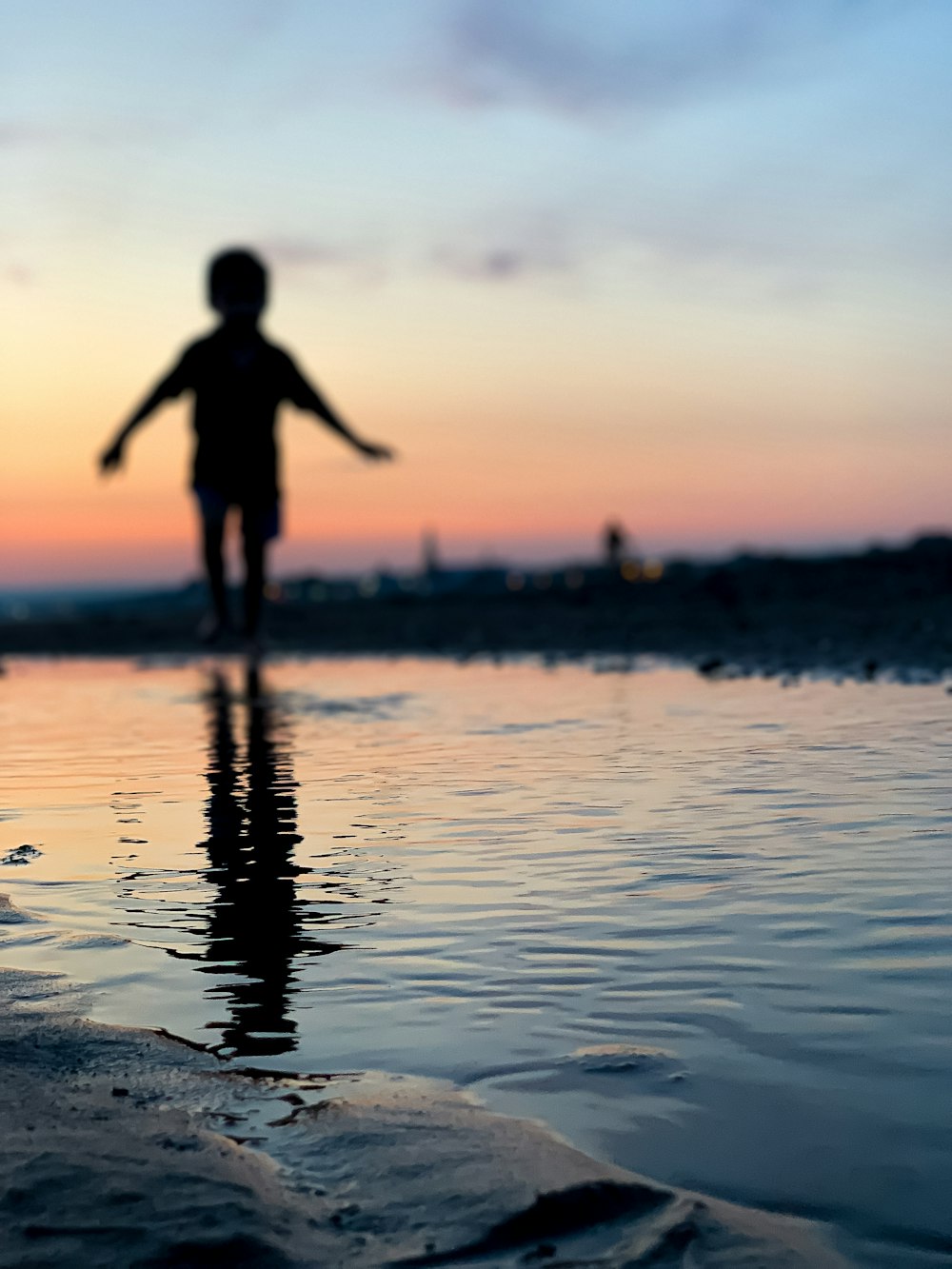 um menino em pé em cima de uma praia ao lado de um corpo de água