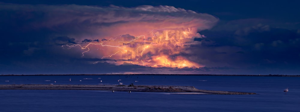 a large cloud filled with lightning over a body of water