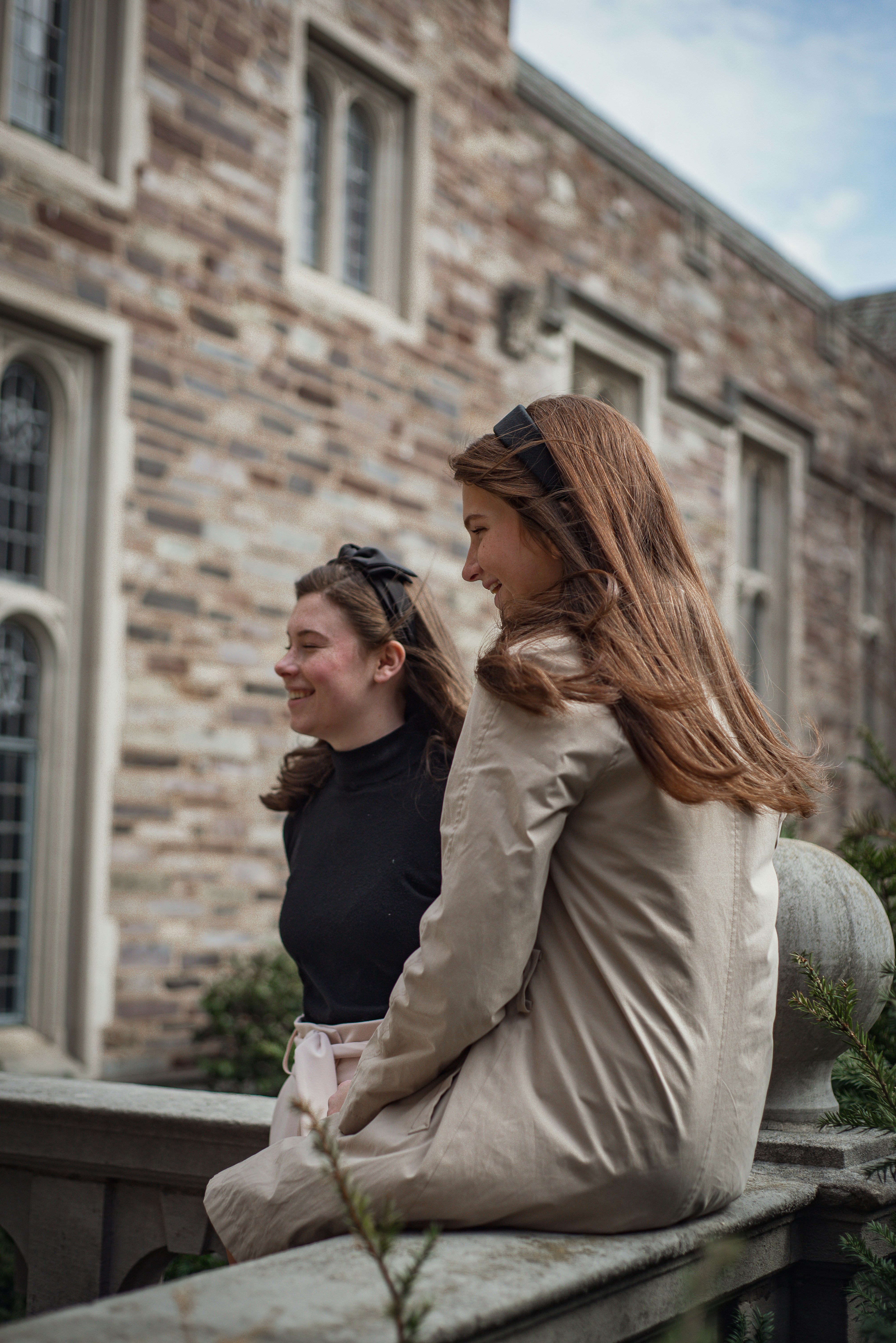 two women sitting on a ledge outside of a building
