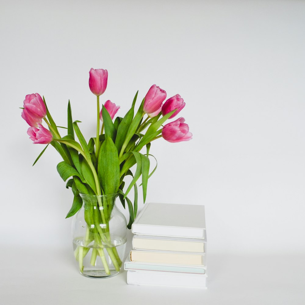 un jarrón de tulipanes rosas junto a una pila de libros