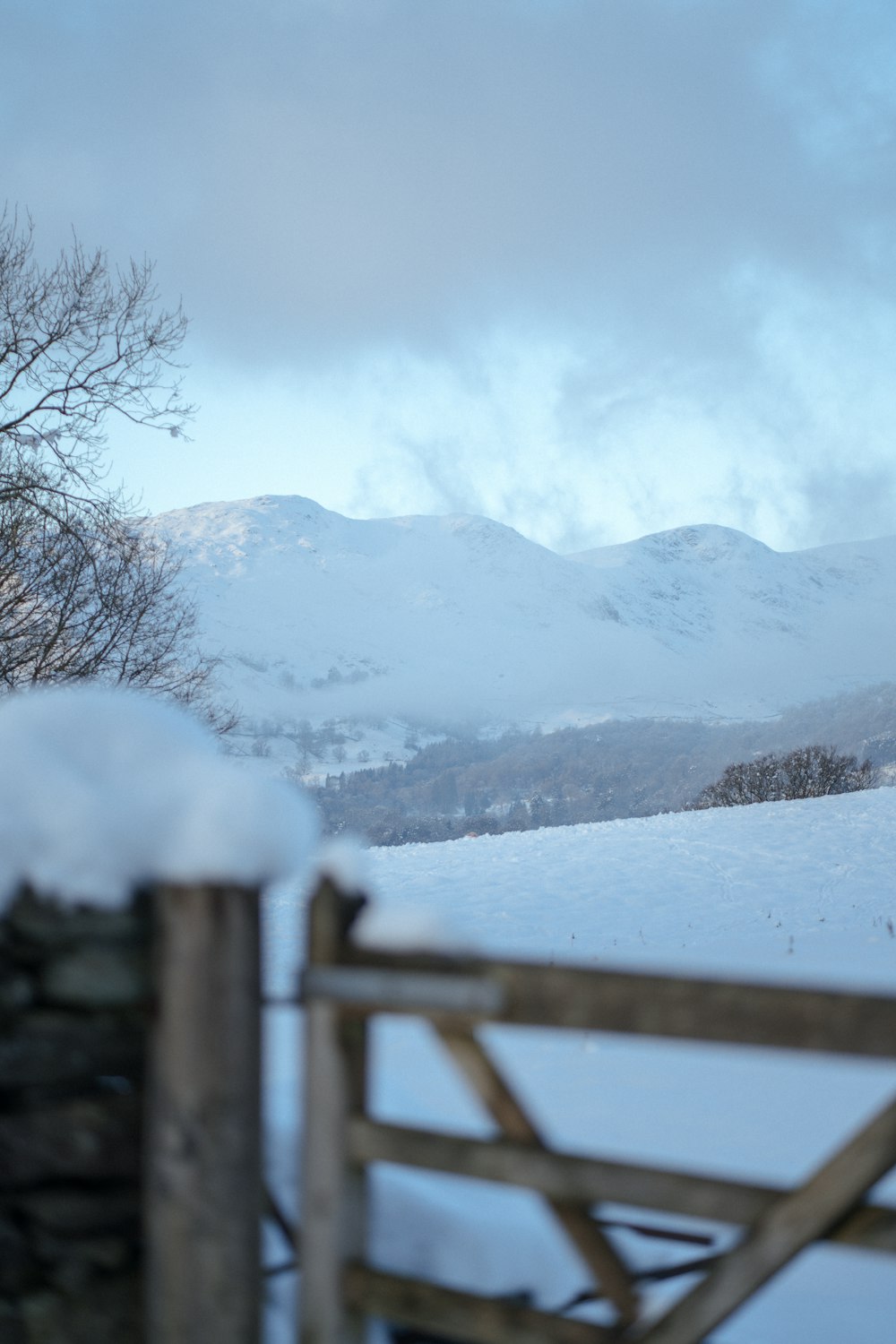 a snow covered field with a fence and mountains in the background