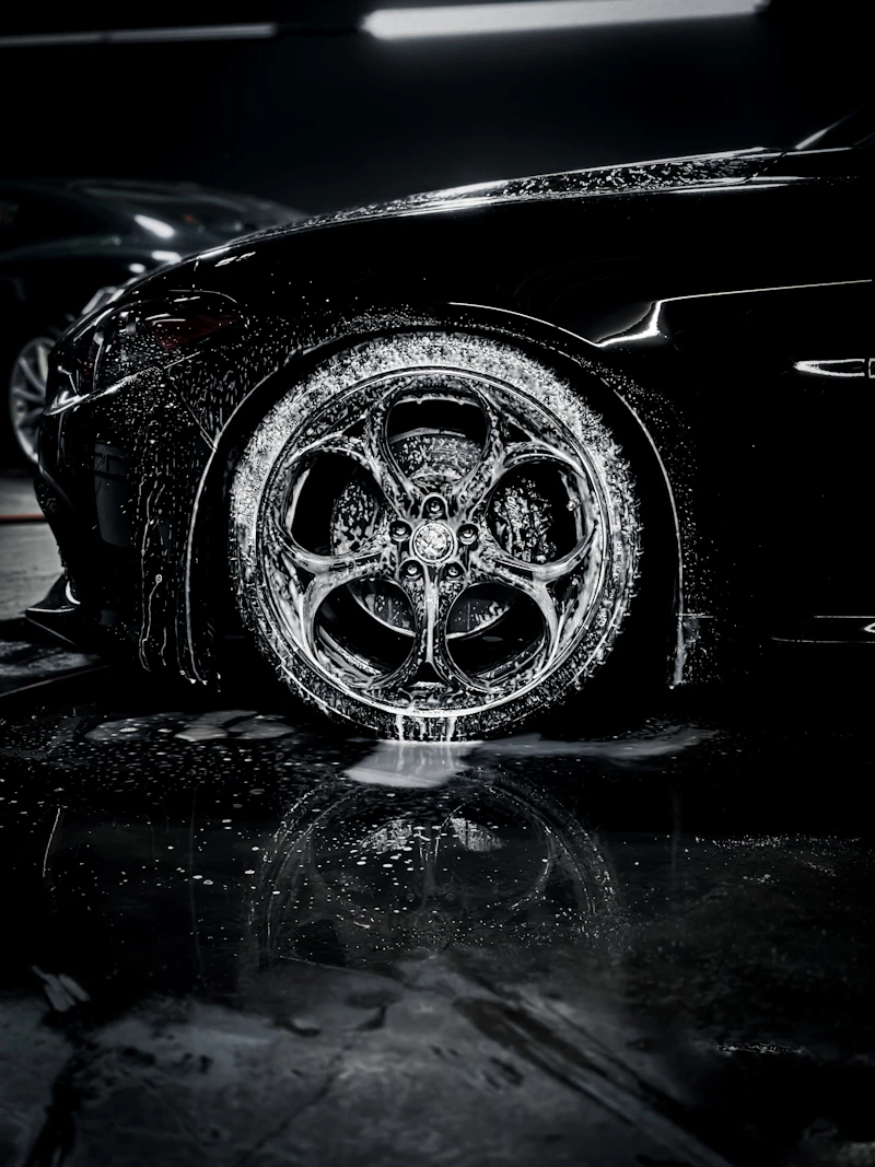 Foam-covered wheel and fender on a dark sports car during the wash stage