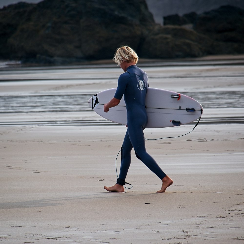 a woman walking on a beach holding a surfboard