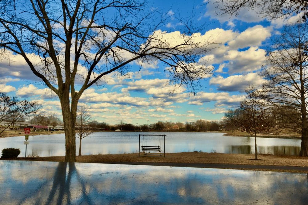 a park bench sitting next to a lake under a cloudy blue sky