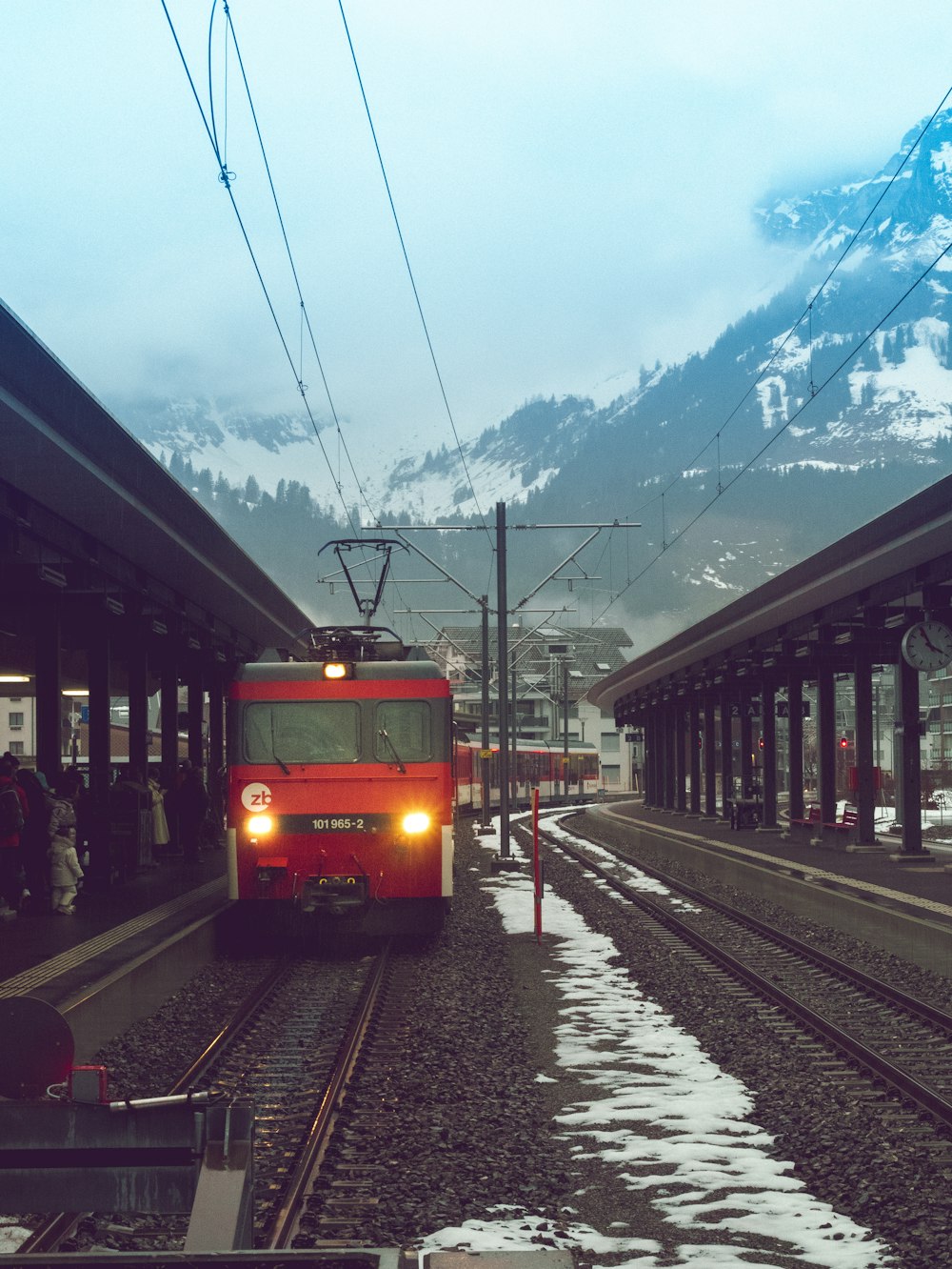 a red train traveling down train tracks next to a snow covered mountain