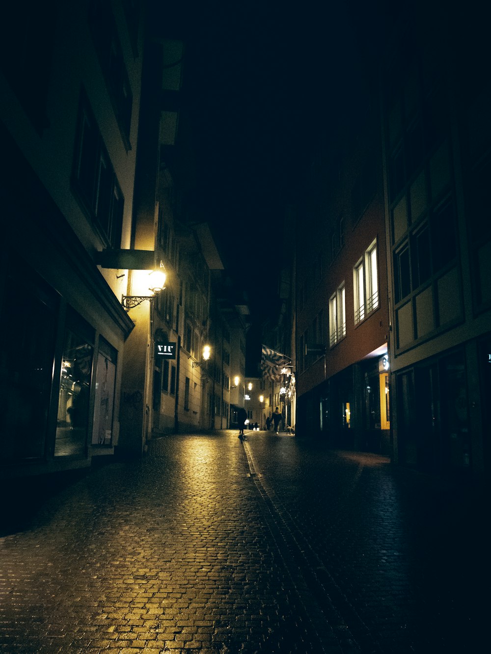 una calle empedrada por la noche con las luces encendidas