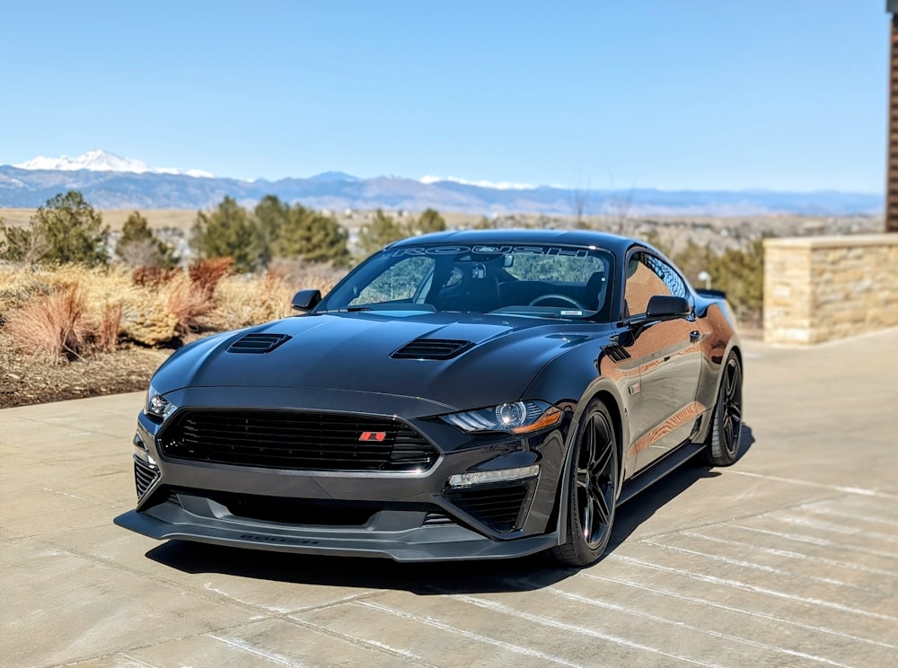 a black mustang parked in a driveway with mountains in the background