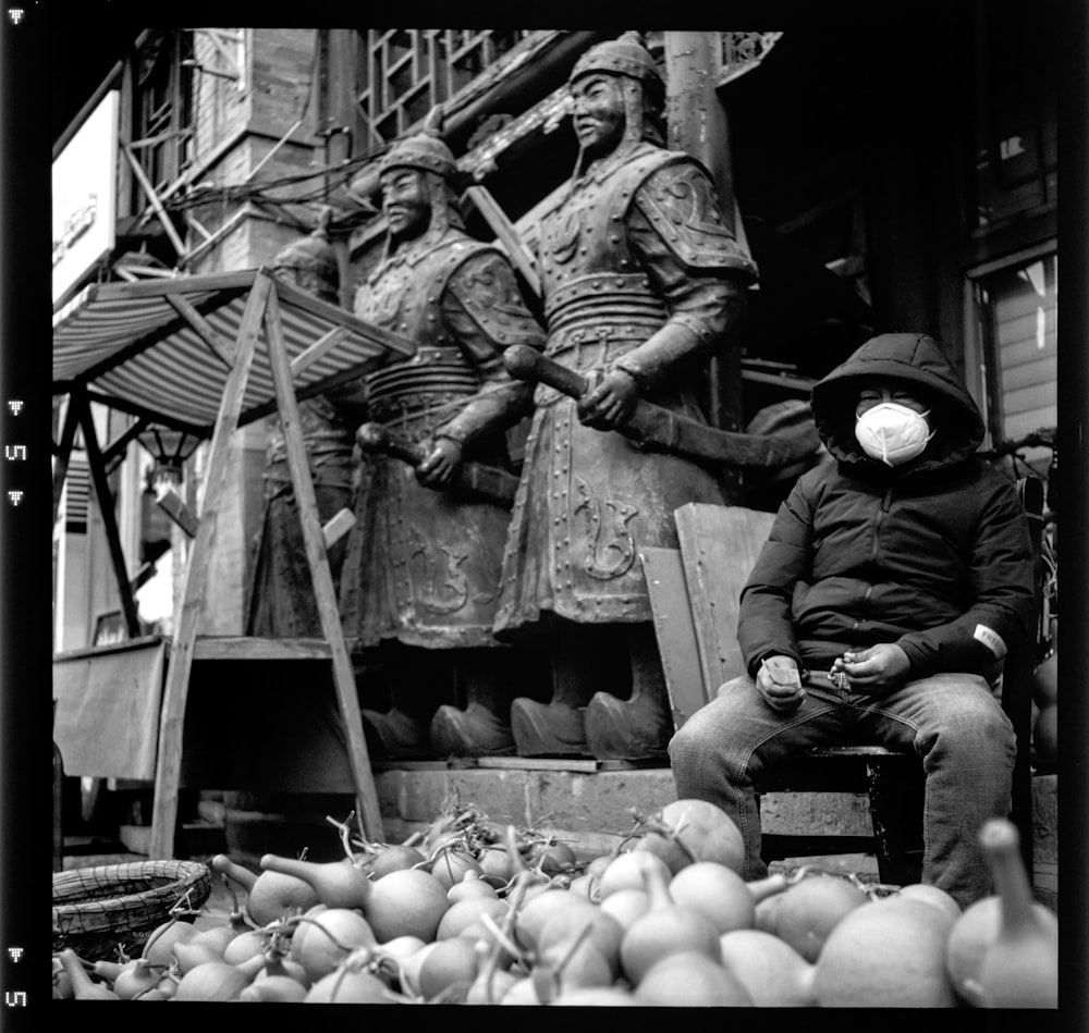 a black and white photo of a man sitting in front of a statue