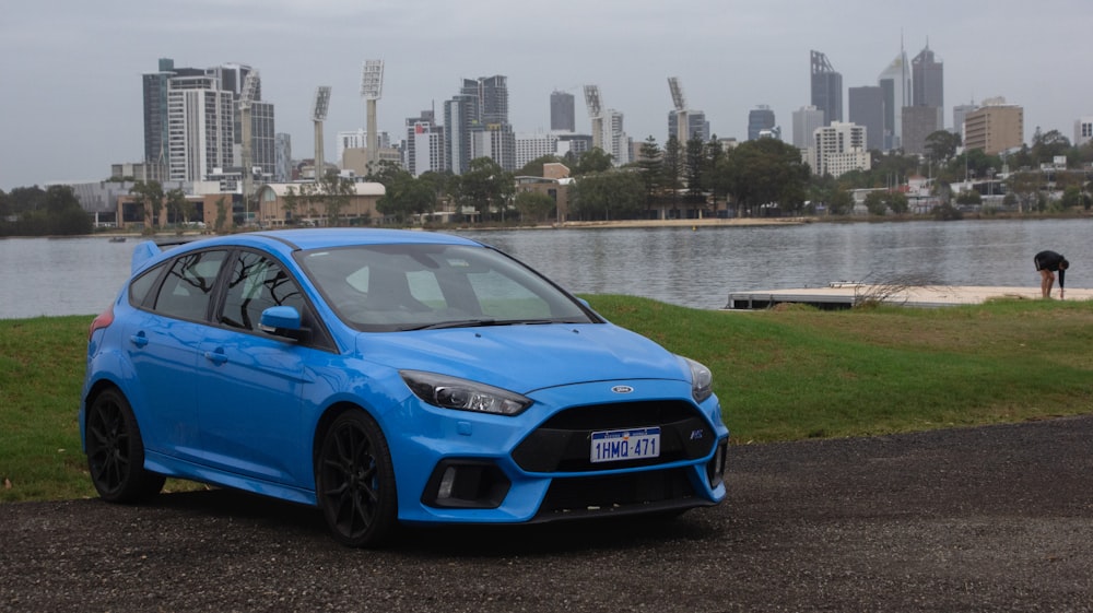 a blue car parked in front of a body of water