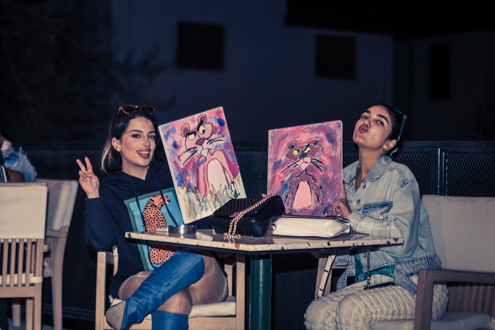 a couple of women sitting at a table with paintings