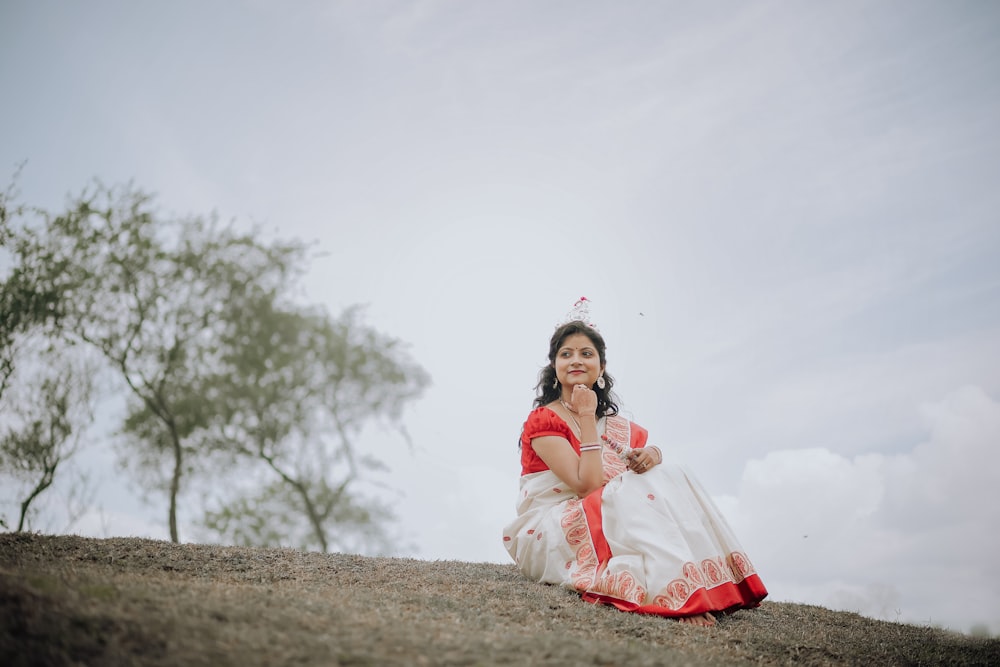 a woman in a red and white dress sitting on a hill