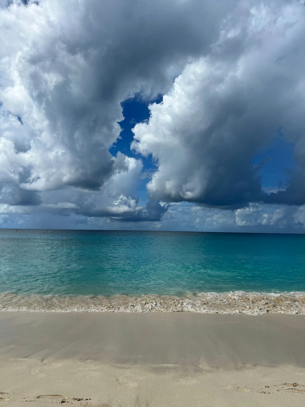 a sandy beach with blue water and clouds in the sky