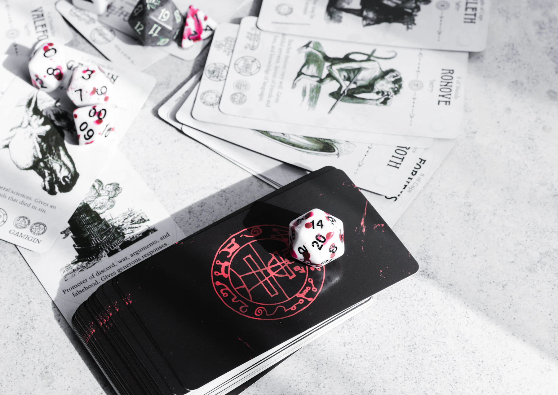 A white twenty-sided die resting on a deck of cards, with more dice and cards behind