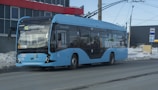 a blue bus driving down a street next to a tall building