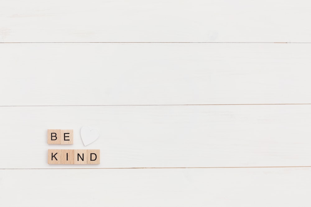 scrabble letters spelling the word be kind on a white background