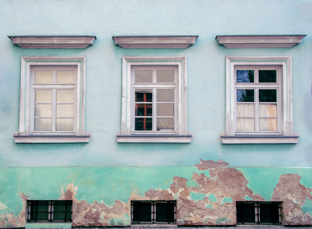 Un edificio azul con tres ventanas y un banco frente a él