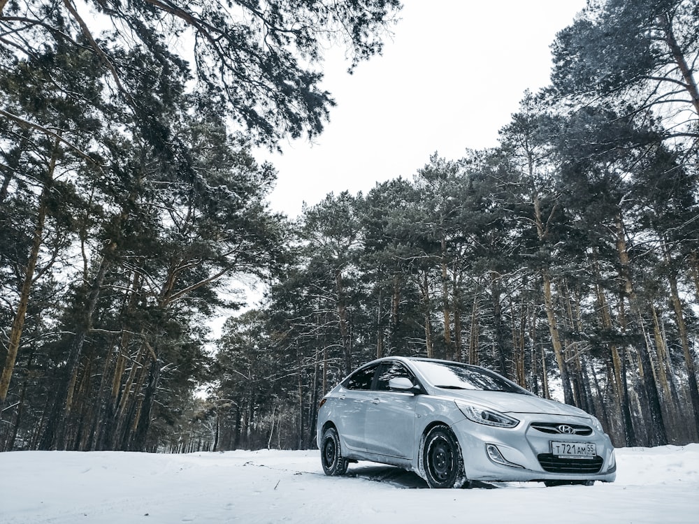 um carro branco estacionado no meio de uma floresta coberta de neve